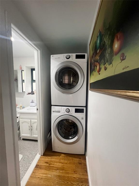 laundry area featuring stacked washer / drying machine, light hardwood / wood-style floors, and sink