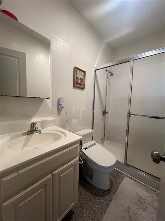 bathroom featuring tile walls, an enclosed shower, vanity, and toilet