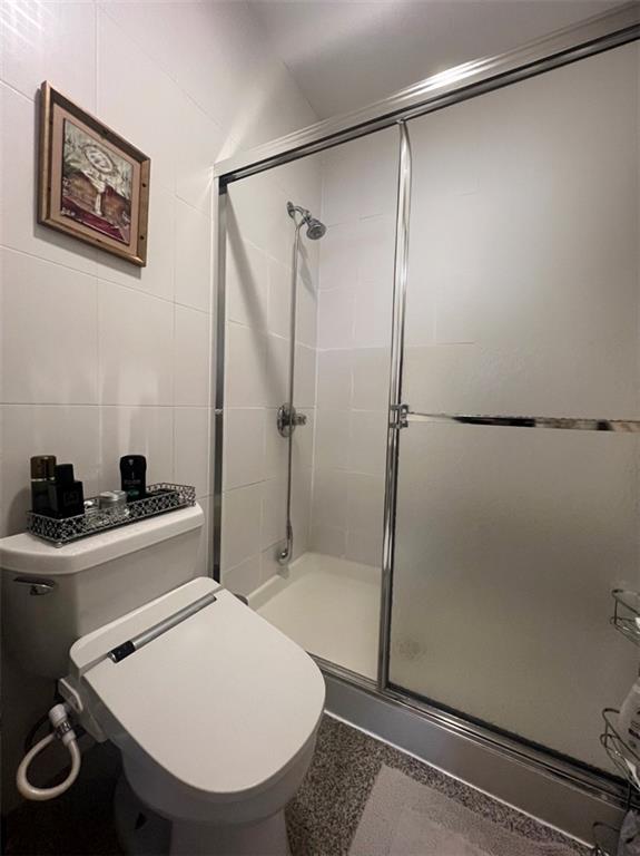 bathroom with tile walls, toilet, and a shower with door