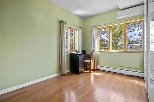 spare room with an AC wall unit, baseboard heating, and light hardwood / wood-style flooring