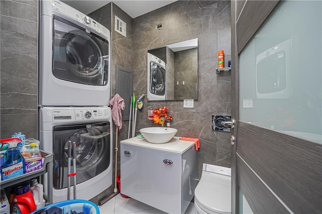 clothes washing area featuring tile patterned floors, stacked washer and clothes dryer, and tile walls