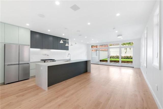 kitchen with sink, pendant lighting, a center island with sink, light hardwood / wood-style flooring, and stainless steel refrigerator