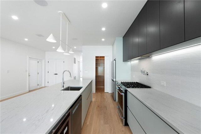 kitchen featuring pendant lighting, sink, light stone countertops, light wood-type flooring, and stainless steel appliances