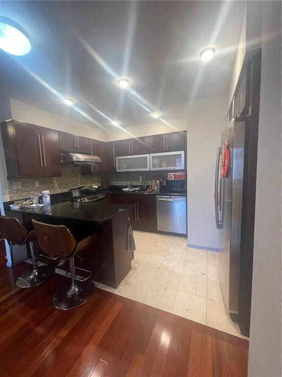 kitchen with a kitchen breakfast bar, decorative backsplash, light wood-type flooring, appliances with stainless steel finishes, and kitchen peninsula