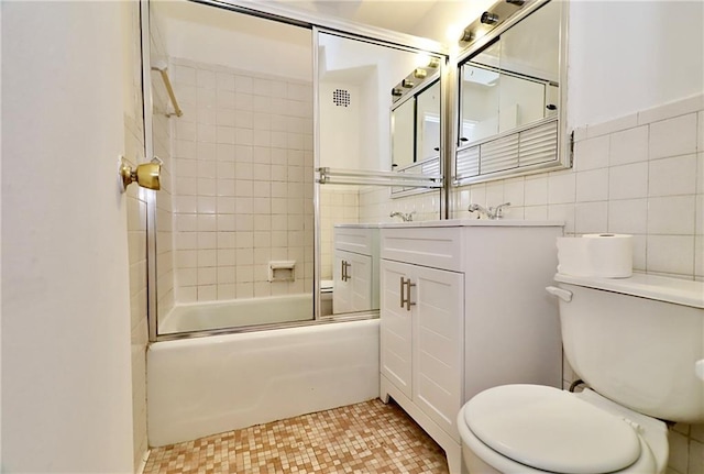 bathroom with visible vents, tile walls, toilet, shower / bath combination with glass door, and vanity