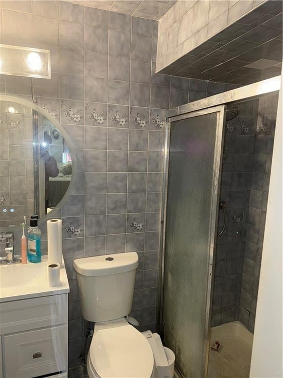 bathroom with tile walls, a shower with door, vanity, and toilet