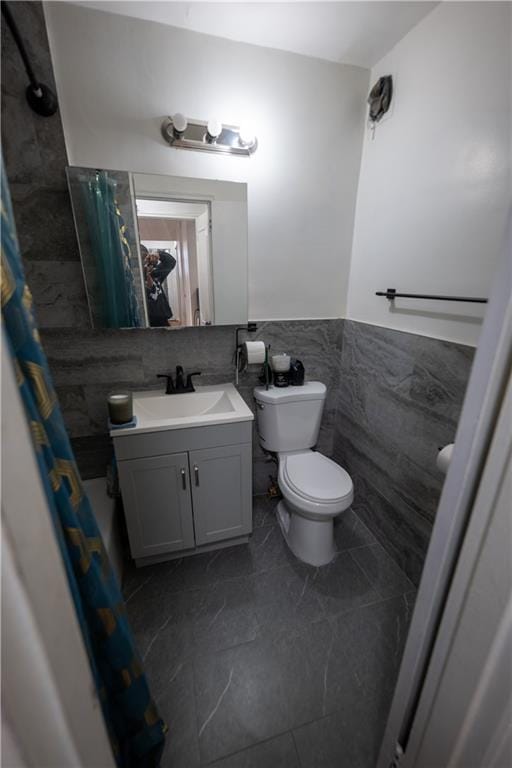 full bathroom featuring vanity, a shower with shower curtain, a wainscoted wall, tile walls, and toilet