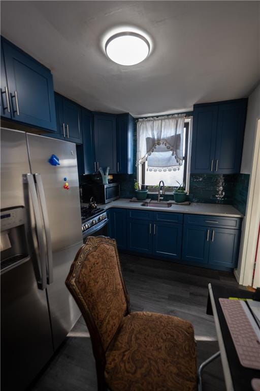 kitchen with a sink, light countertops, appliances with stainless steel finishes, blue cabinets, and tasteful backsplash