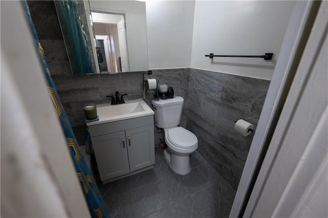 bathroom featuring vanity, a wainscoted wall, tile walls, toilet, and tile patterned floors