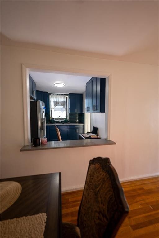 kitchen featuring blue cabinets, wood finished floors, freestanding refrigerator, and a sink