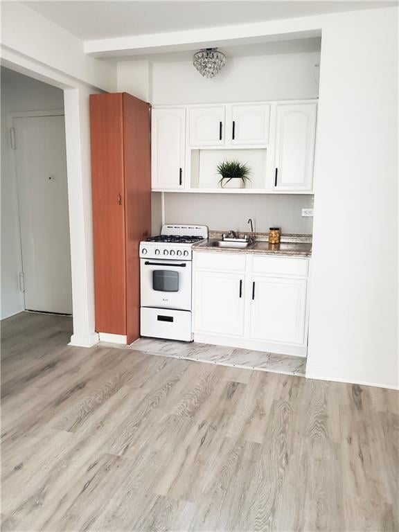 kitchen featuring white cabinetry, sink, light hardwood / wood-style floors, and white gas stove