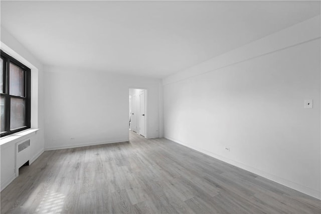 spare room featuring radiator and light hardwood / wood-style flooring