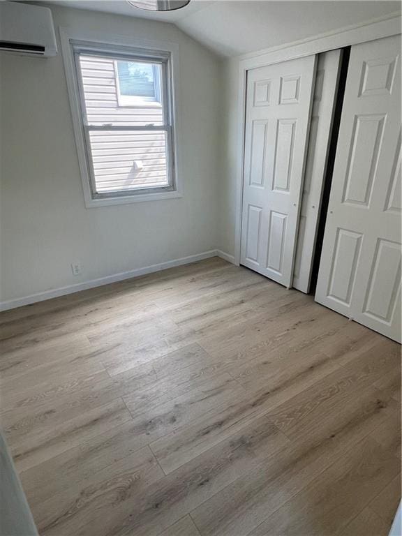 unfurnished bedroom with a wall unit AC, vaulted ceiling, and light hardwood / wood-style flooring