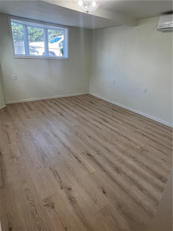 unfurnished room featuring a wall mounted AC, an inviting chandelier, and light hardwood / wood-style floors