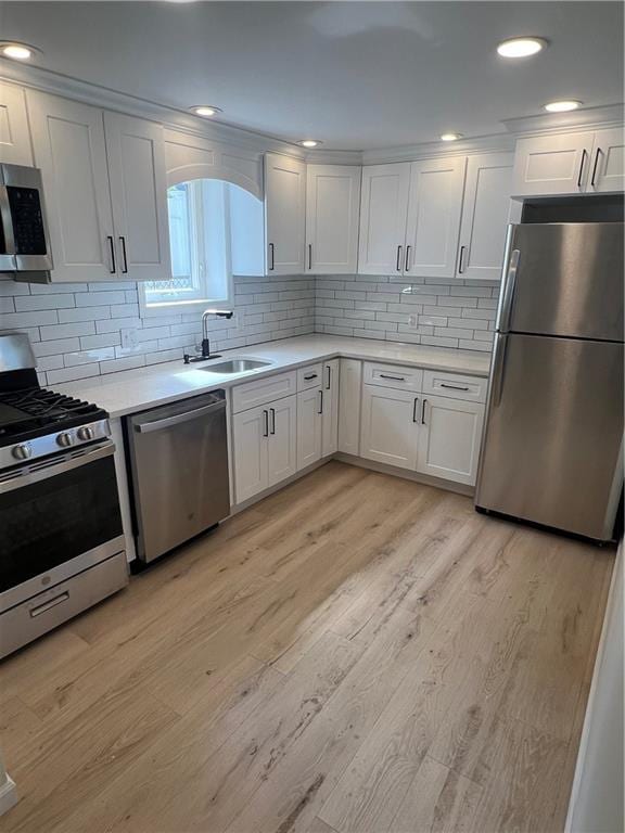 kitchen featuring white cabinets, stainless steel appliances, decorative backsplash, sink, and light wood-type flooring