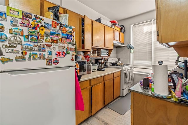 kitchen featuring light wood-type flooring, backsplash, and white appliances