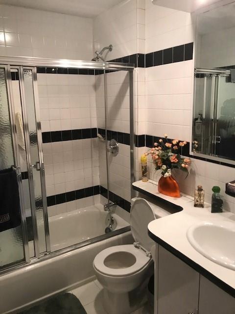 full bathroom featuring tile patterned floors, toilet, shower / bath combination with glass door, decorative backsplash, and vanity