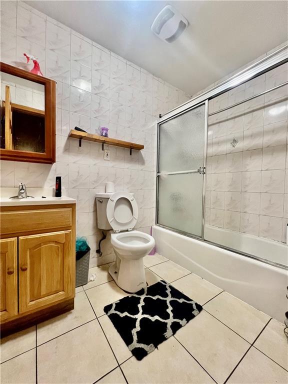 full bathroom with shower / bath combination with glass door, tile walls, toilet, vanity, and tile patterned floors