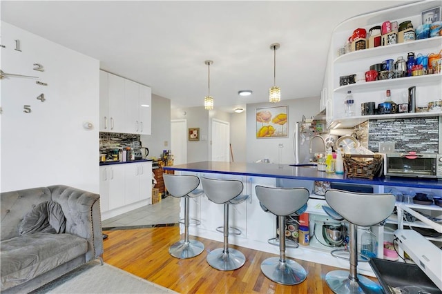 kitchen featuring white cabinetry, sink, decorative light fixtures, decorative backsplash, and light wood-type flooring