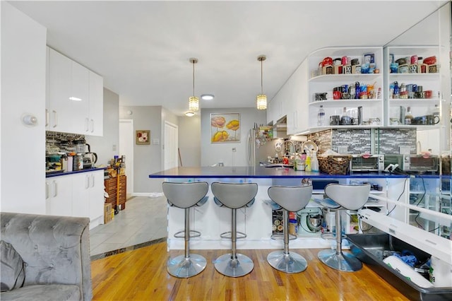 kitchen with white cabinets, hanging light fixtures, decorative backsplash, stainless steel fridge, and light tile patterned flooring