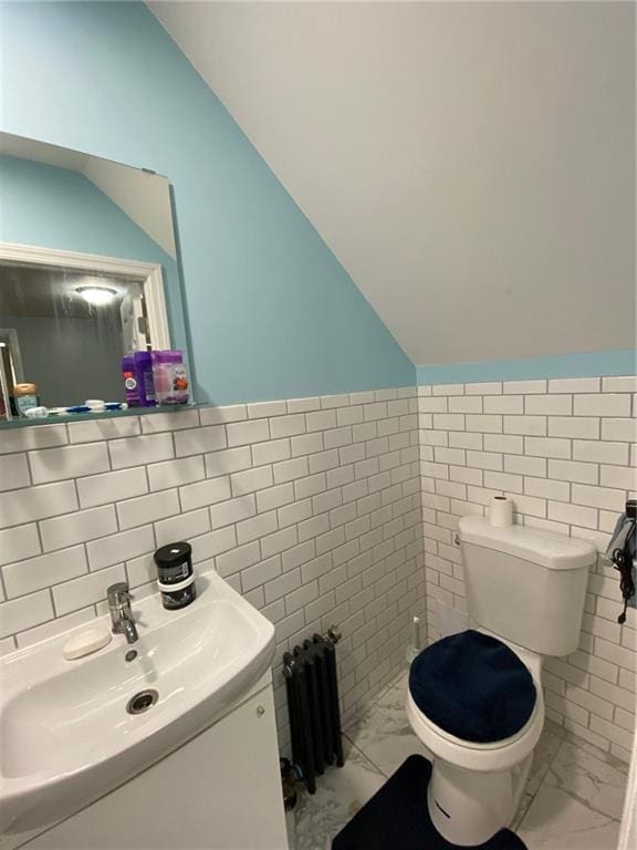 bathroom with radiator, vanity, tile walls, toilet, and lofted ceiling