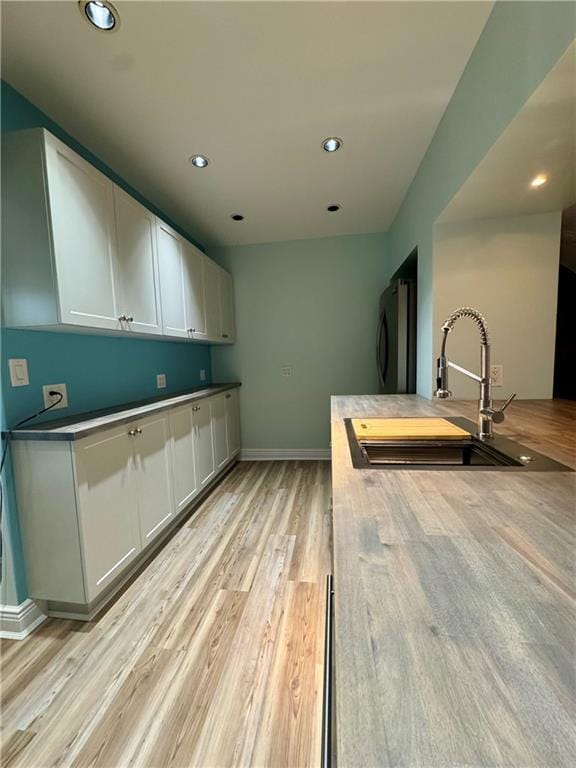 kitchen featuring refrigerator, light wood-style flooring, recessed lighting, a sink, and white cabinetry