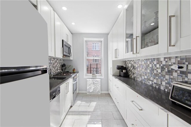 kitchen with white cabinetry, tasteful backsplash, dark stone counters, light tile patterned floors, and appliances with stainless steel finishes