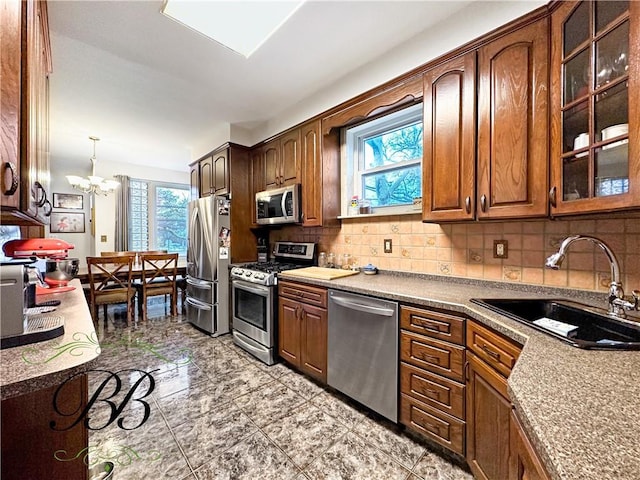 kitchen featuring pendant lighting, backsplash, sink, appliances with stainless steel finishes, and a chandelier