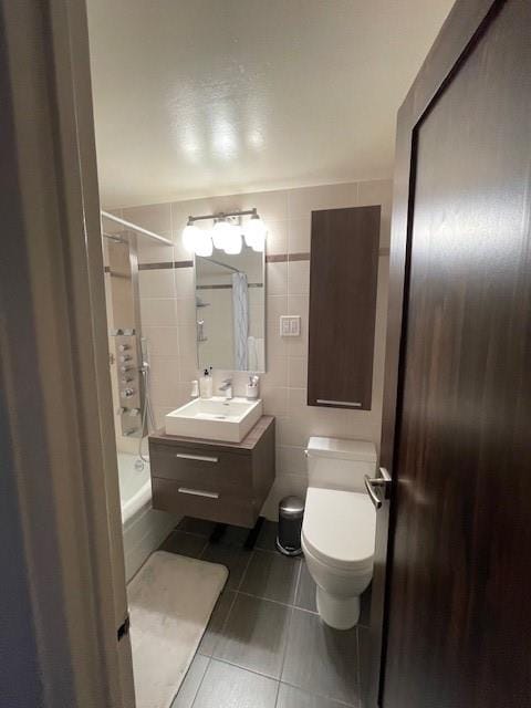 full bathroom with tile walls, shower / bathtub combination with curtain, vanity, tile patterned flooring, and toilet