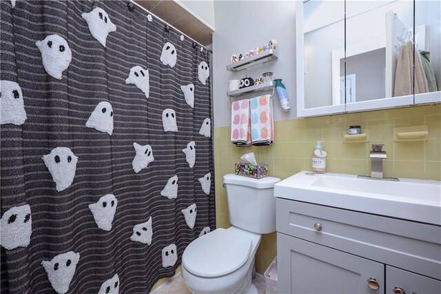 bathroom with decorative backsplash, tile walls, vanity, and toilet