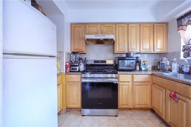 kitchen featuring light tile patterned floors, tasteful backsplash, gas range, light brown cabinetry, and white fridge