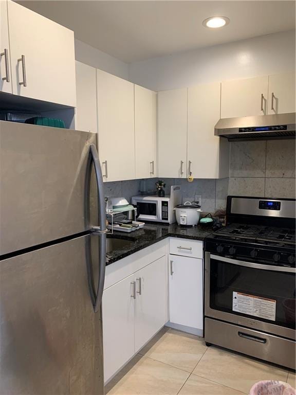 kitchen with tasteful backsplash, white cabinets, appliances with stainless steel finishes, light tile patterned floors, and dark stone countertops