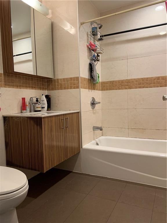 full bathroom featuring tile walls, tile patterned floors, tiled shower / bath, vanity, and toilet