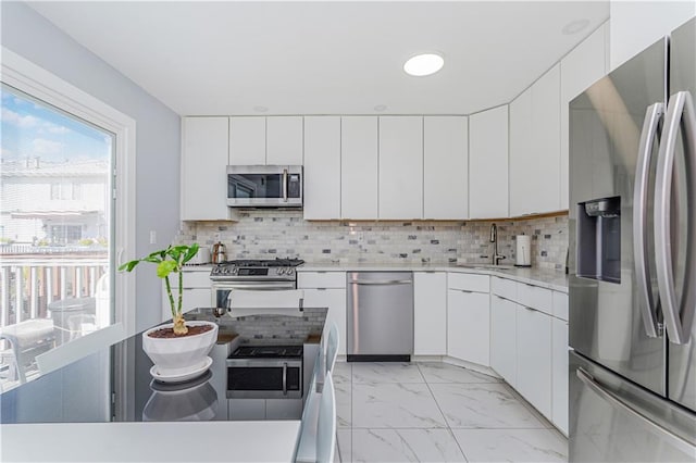 kitchen featuring decorative backsplash, white cabinets, stainless steel appliances, and sink