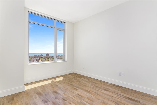 empty room with light wood-type flooring, a water view, and baseboards