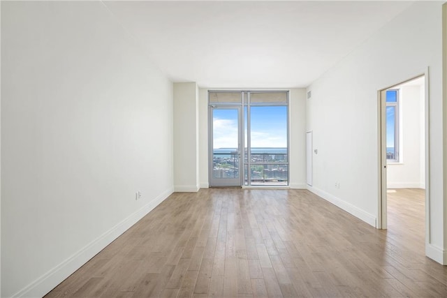 spare room featuring baseboards, floor to ceiling windows, and light wood finished floors