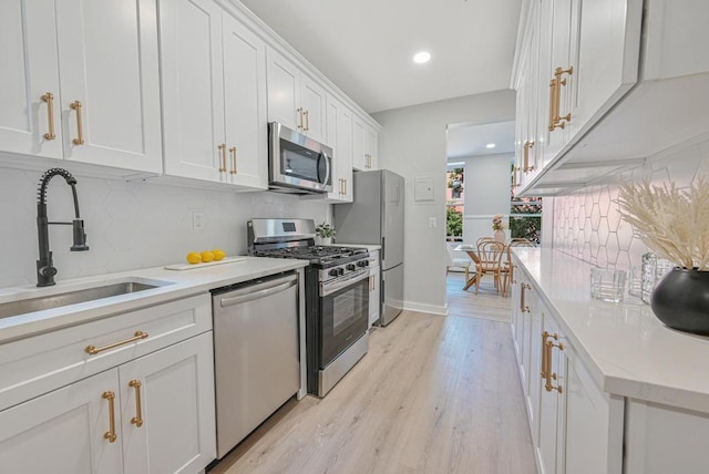 kitchen featuring appliances with stainless steel finishes, light wood-type flooring, sink, white cabinetry, and backsplash