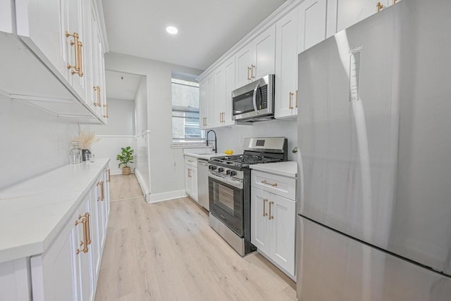 kitchen with white cabinets, stainless steel appliances, light countertops, and light wood-style floors