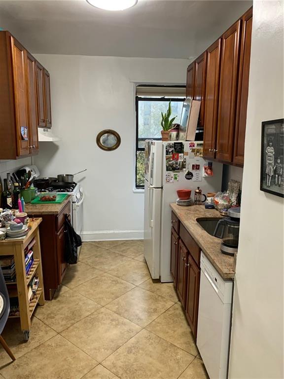 kitchen featuring light stone counters, white appliances, sink, light tile patterned floors, and range hood