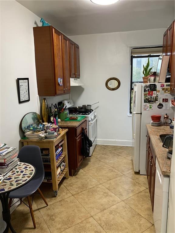 kitchen with light tile patterned floors, light stone counters, white appliances, and exhaust hood