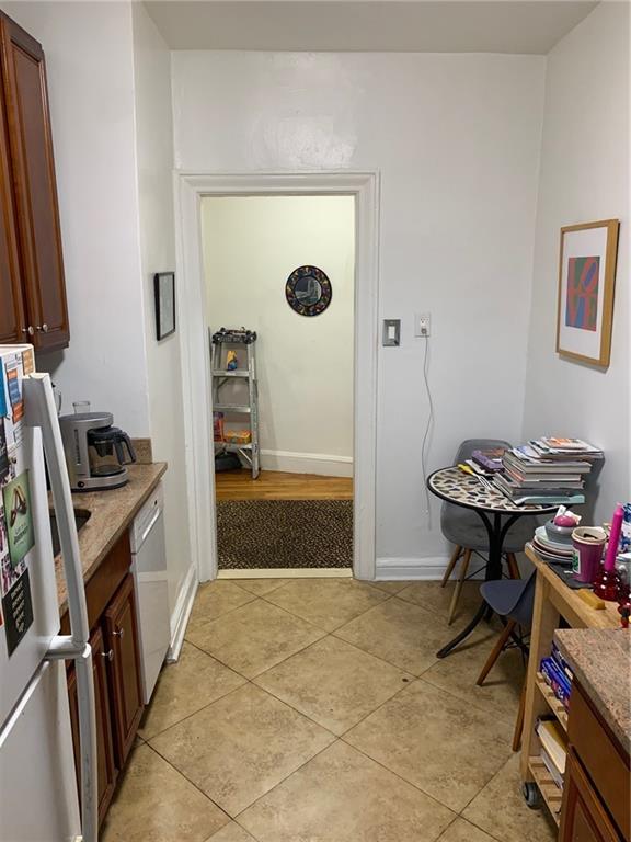 kitchen featuring freestanding refrigerator, dishwasher, baseboards, and light tile patterned floors