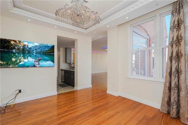 unfurnished living room featuring a chandelier, light wood-type flooring, baseboards, and a sink