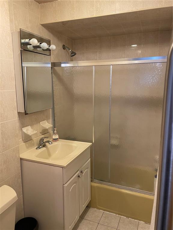 full bathroom with vanity, tile walls, enclosed tub / shower combo, tile patterned flooring, and toilet