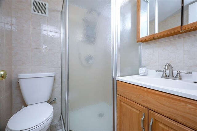 bathroom featuring a shower with door, tile walls, vanity, decorative backsplash, and toilet