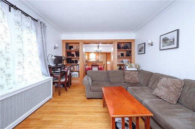 living room featuring built in shelves, crown molding, light hardwood / wood-style flooring, radiator, and a notable chandelier