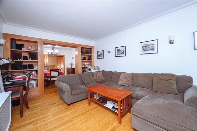 living room with an inviting chandelier, ornamental molding, built in shelves, and light hardwood / wood-style floors