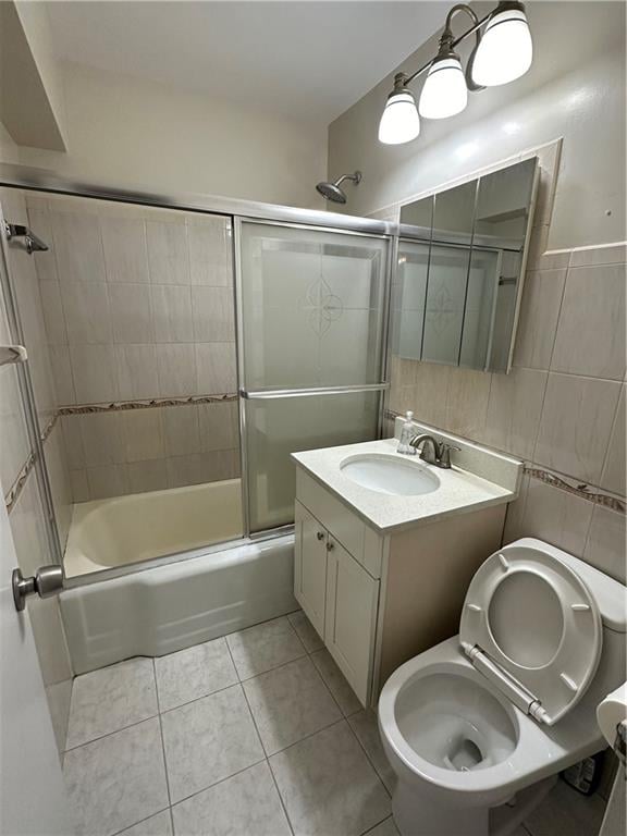 full bathroom featuring tile patterned floors, toilet, bath / shower combo with glass door, tile walls, and vanity