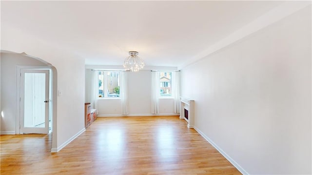 empty room with arched walkways, baseboards, an inviting chandelier, and light wood-style floors