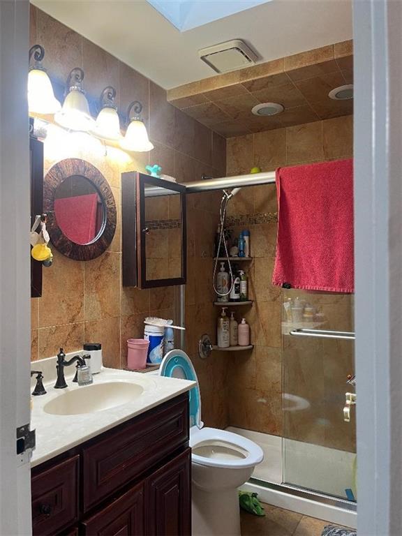 bathroom featuring vanity, tile walls, toilet, and a shower with door