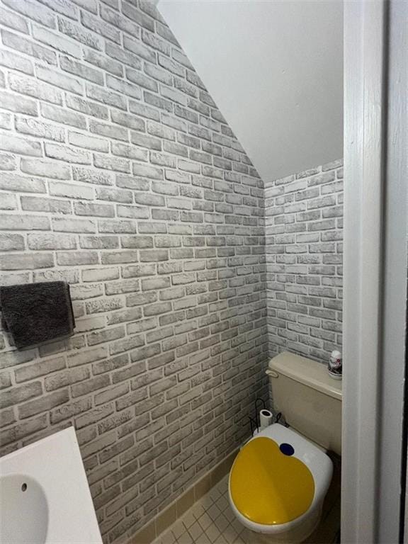 bathroom featuring brick wall, lofted ceiling, toilet, and tile patterned floors